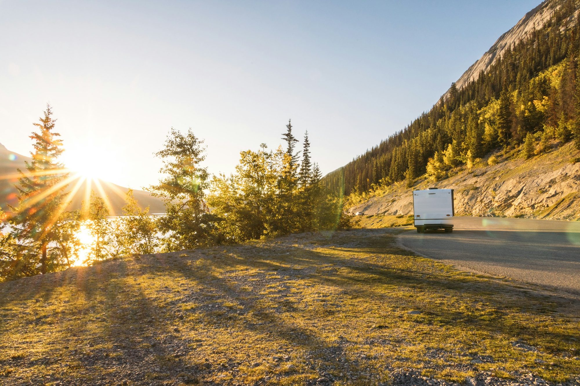 Een camper rijdt bij zonsondergang over een bergweg langs een meer