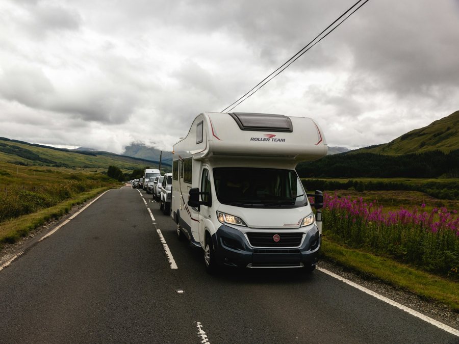 Een camper op een smalle weg door de heuvels, met verkeer erachter